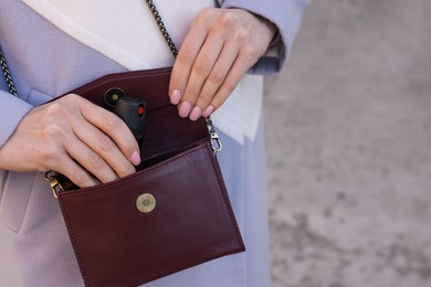 Photo of Young woman putting pepper spray into bag outdoors, closeup. Space for text