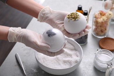 Photo of Woman in gloves with self made bath bombs at grey table, closeup