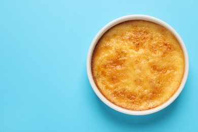 Photo of Delicious creme brulee in ceramic ramekin on light blue background, top view. Space for text