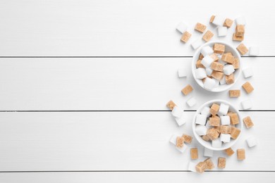 Different sugar cubes in bowls on white wooden table, flat lay. Space for text