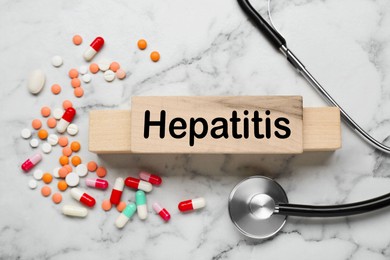 Photo of Word Hepatitis made of wooden cubes, stethoscope and pills on white marble table, flat lay
