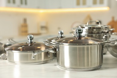 Photo of Set of shiny cooking utensils on white table against blurred background