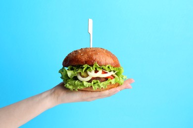 Photo of Woman holding delicious vegetarian burger on light blue background, closeup