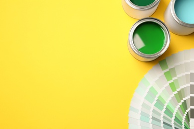 Photo of Paint cans and color palette on yellow background, top view. Space for text