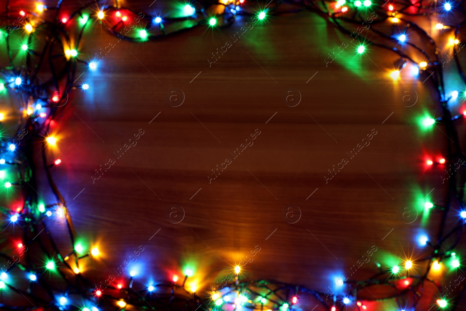 Photo of Blurred view of frame made with colorful Christmas lights on wooden background