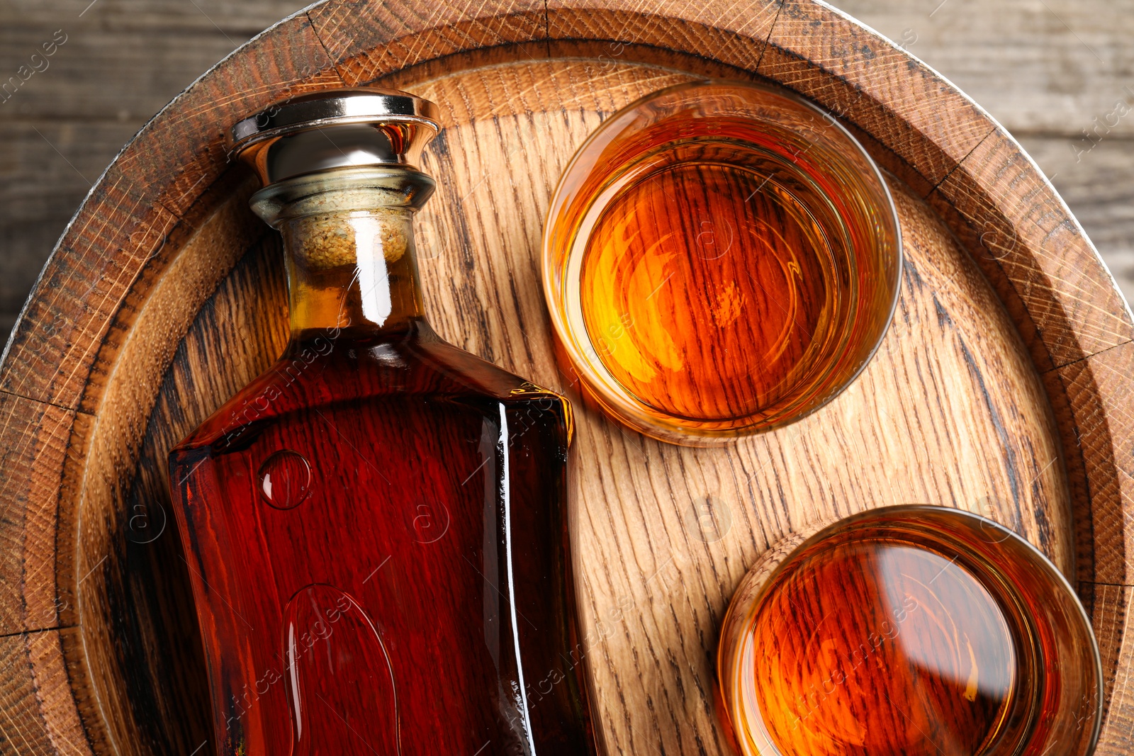 Photo of Glasses and bottle of whiskey on wooden barrel, flat lay