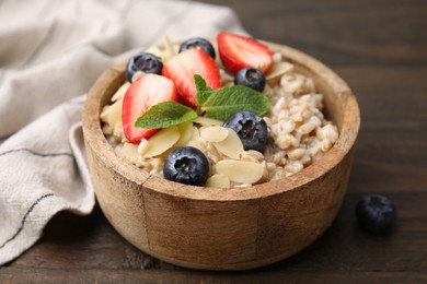 Photo of Tasty oatmeal with strawberries, blueberries and almond petals in bowl on wooden table, closeup