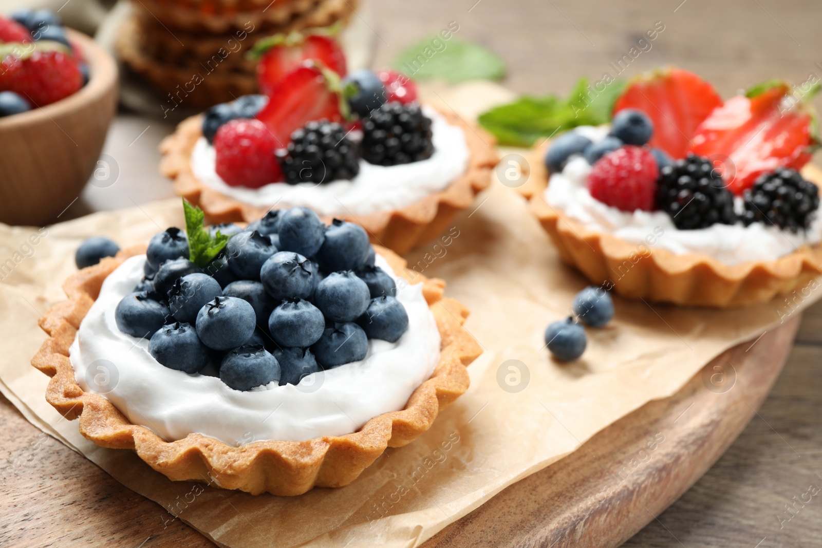 Photo of Different berry tarts on wooden table. Delicious pastries