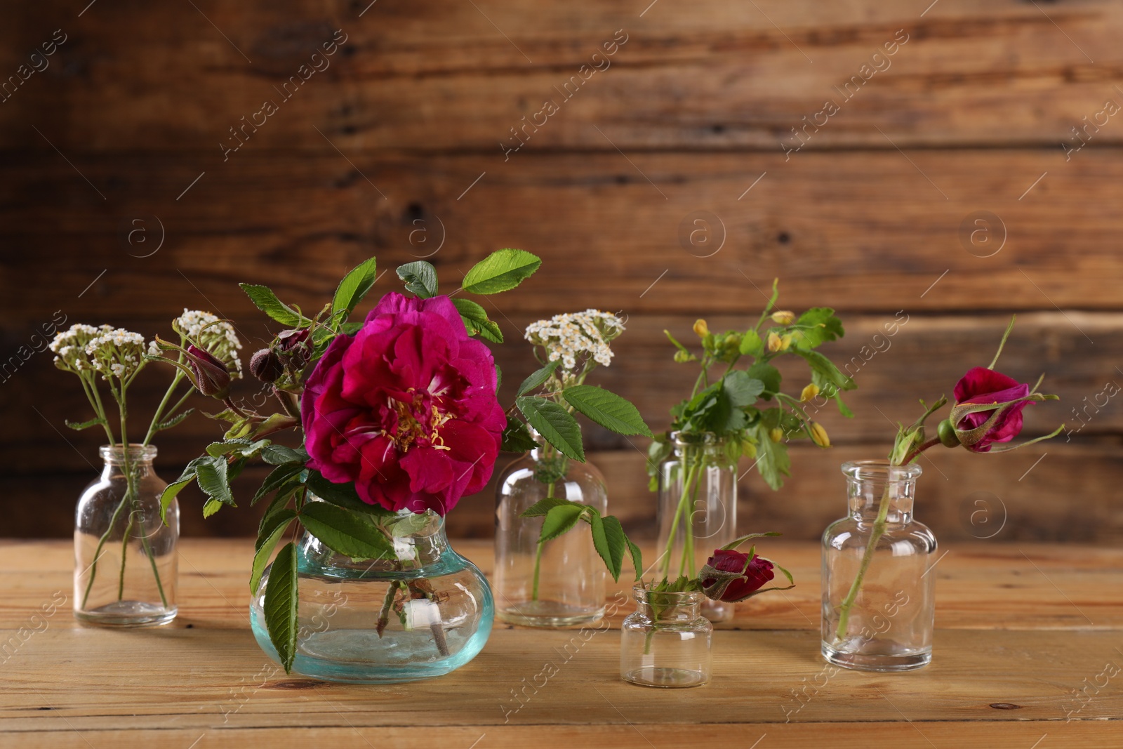 Photo of Different flowers in glass bottles on wooden table