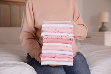 Photo of Woman holding stack of girl's clothes in bedroom, closeup