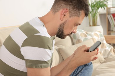 Photo of Man with poor posture using smartphone on sofa at home