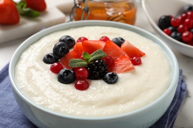 Photo of Delicious semolina pudding with berries in bowl on table, closeup