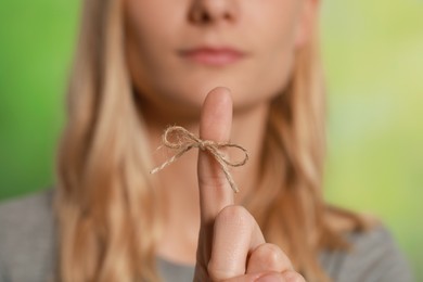 Woman showing index finger with tied bow as reminder against green blurred background, focus on hand