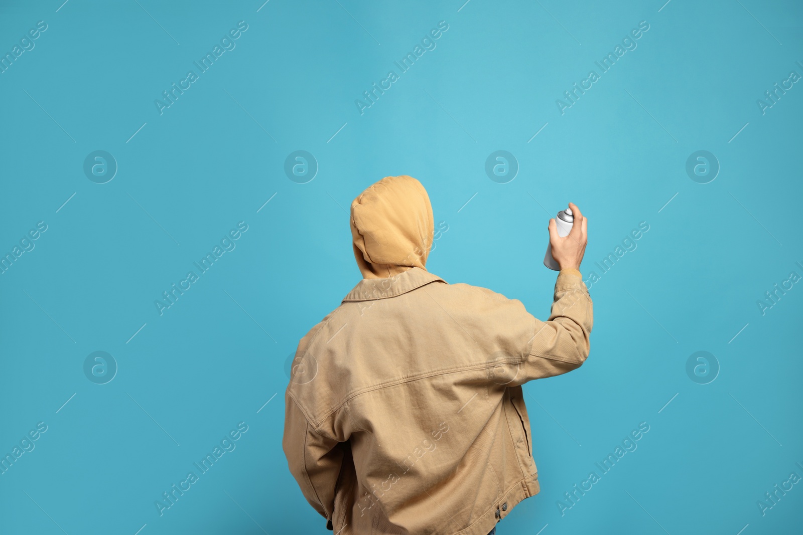 Photo of Man holding white can of spray paint on light blue background, back view