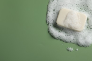 Photo of Soap and fluffy foam on green background, top view. Space for text