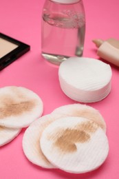 Dirty cotton pads after removing makeup and different cosmetic products on pink background, closeup