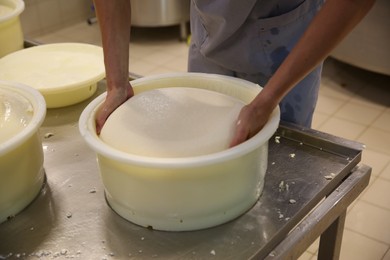 Worker taking fresh cheese from mould at modern factory, closeup