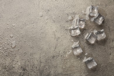 Photo of Melting ice cubes and water drops on grey textured table, flat lay. Space for text