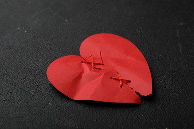 Photo of Torn paper heart sewed with thread on black stone background. Relationship problems concept