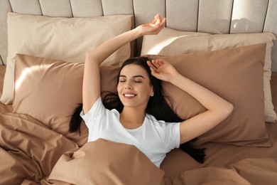 Photo of Young woman lying in bed with brown linens at home, above view