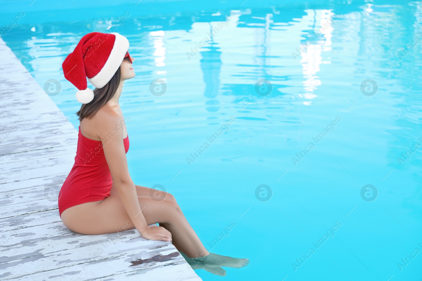 Photo of Young woman wearing Santa Claus hat near swimming pool, space for text. Christmas vacation