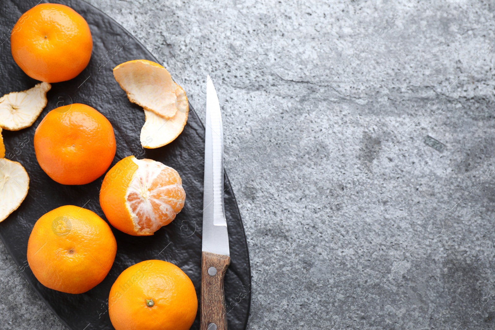 Photo of Fresh ripe tangerines and knife on grey table, top view. Space for text