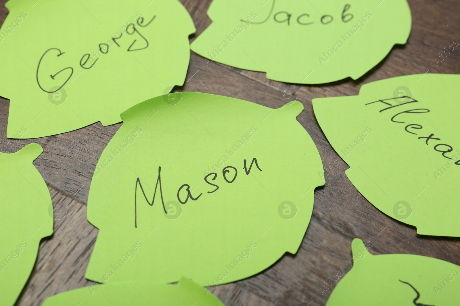 Photo of Paper stickers with different names on wooden table, closeup. Choosing baby's name