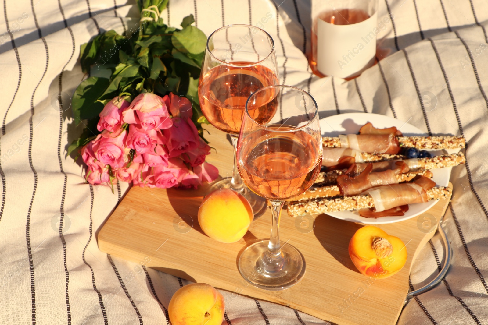 Photo of Glasses of delicious rose wine, flowers and food on white picnic blanket