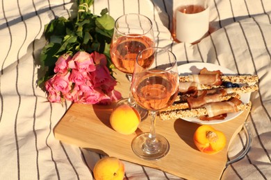 Glasses of delicious rose wine, flowers and food on white picnic blanket