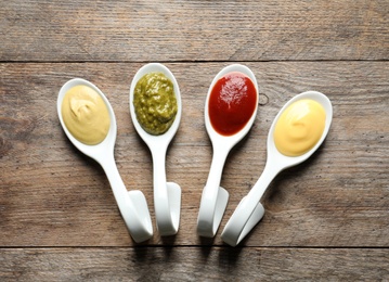 Photo of Spoons with different sauces on wooden background, flat lay