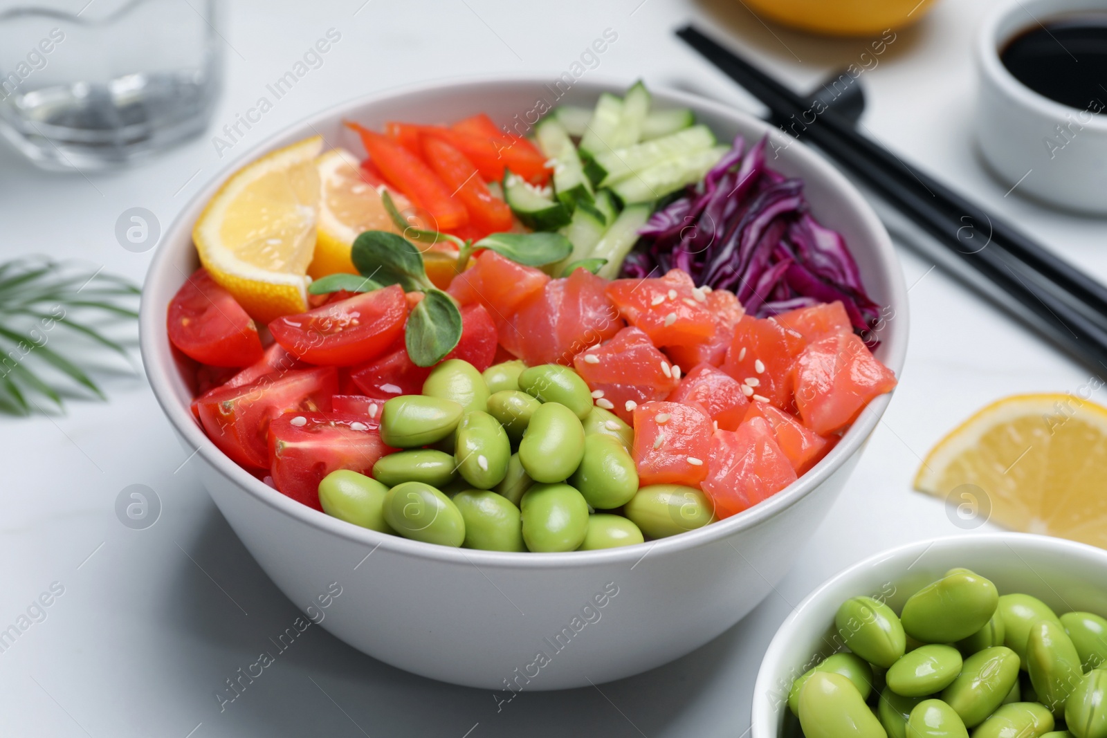 Photo of Poke bowl with salmon, edamame beans and vegetables on white table