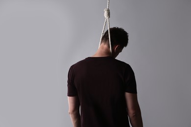 Photo of Man with rope noose on neck against light grey background, back view