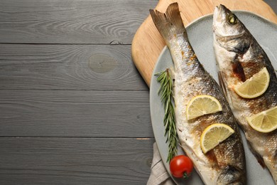 Photo of Delicious baked fish, tomato, lemon and rosemary on grey wooden table, top view. Space for text