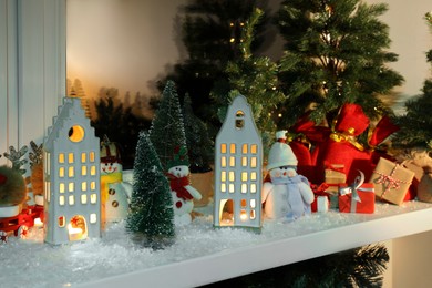 Christmas atmosphere. Beautiful glowing houses, fir trees and toys on window sill indoors