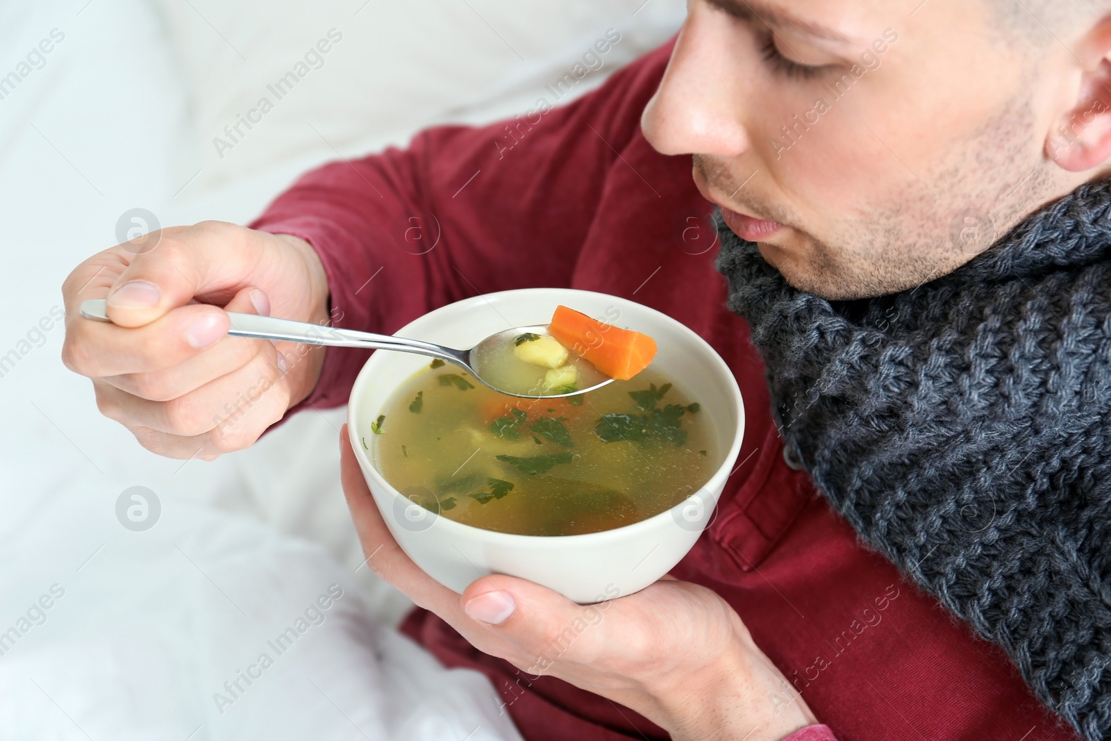 Photo of Sick young man eating broth to cure cold in bed at home