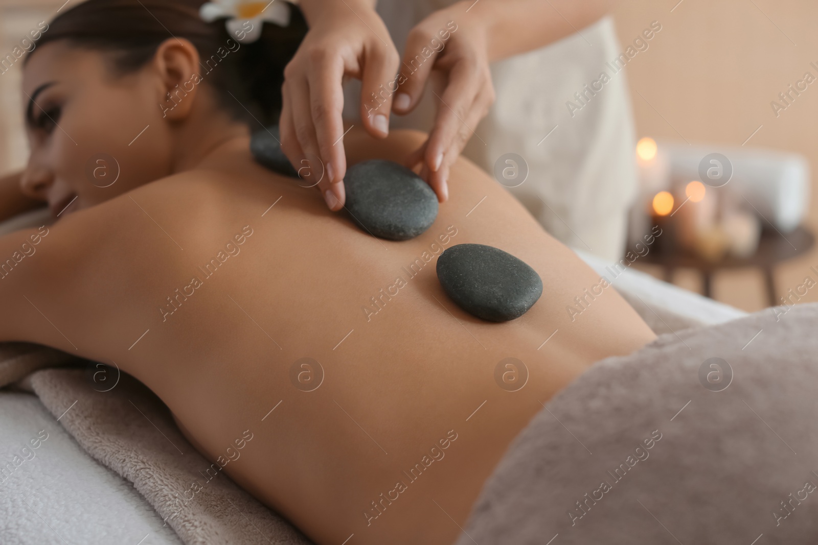 Photo of Beautiful young woman getting hot stone massage in spa salon