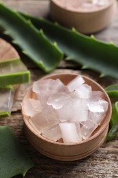 Photo of Aloe vera gel and slices of plant on wooden table, closeup