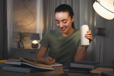 Photo of Young woman with energy drink studying at home