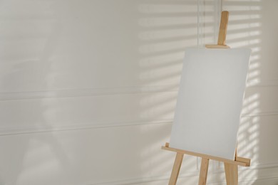 Wooden easel with blank canvas on light background. Space for text