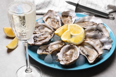 Photo of Fresh oysters with lemon and glass of champagne on grey table, closeup