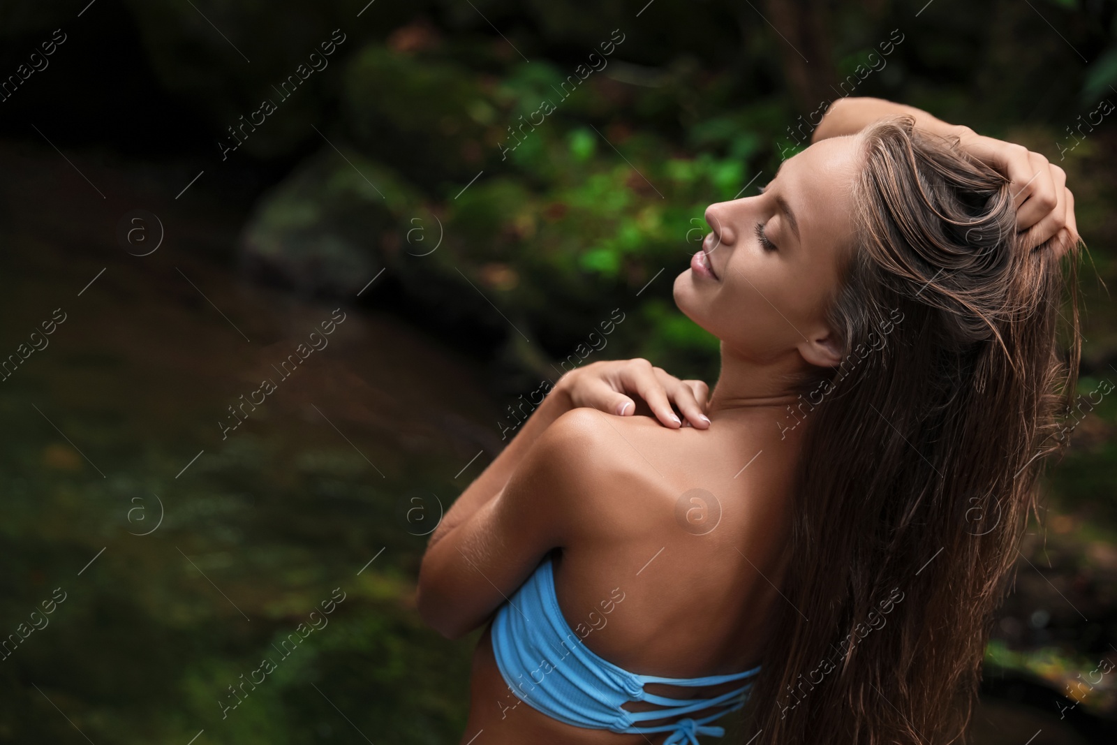 Photo of Beautiful young woman in light blue bikini relaxing near mountain river outdoors. Space for text