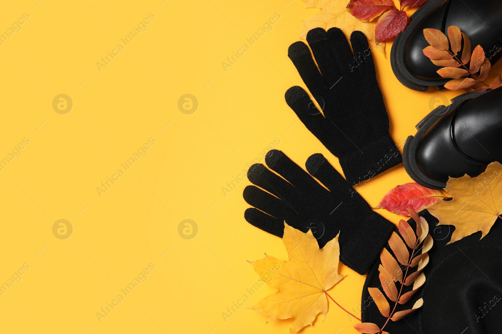 Photo of Stylish woolen gloves, pair of shoes and dry leaves on yellow background, flat lay. Space for text
