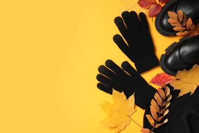 Stylish woolen gloves, pair of shoes and dry leaves on yellow background, flat lay. Space for text