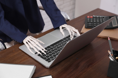 Photo of Human skeleton in suit using laptop at table, closeup