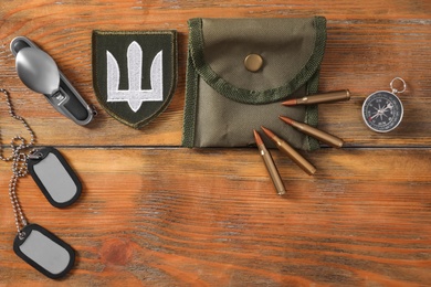 Photo of MYKOLAIV, UKRAINE - SEPTEMBER 26, 2020: Tactical gear and Ukrainian army patch on wooden table, flat lay. Space for text