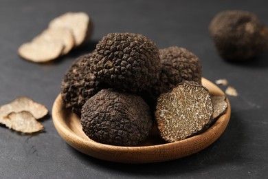Photo of Black truffles in wooden plate on grey table, closeup