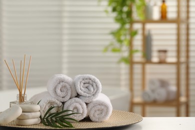 Photo of Spa composition. Towels, reed diffuser, stones and palm leaves on white table in bathroom, space for text