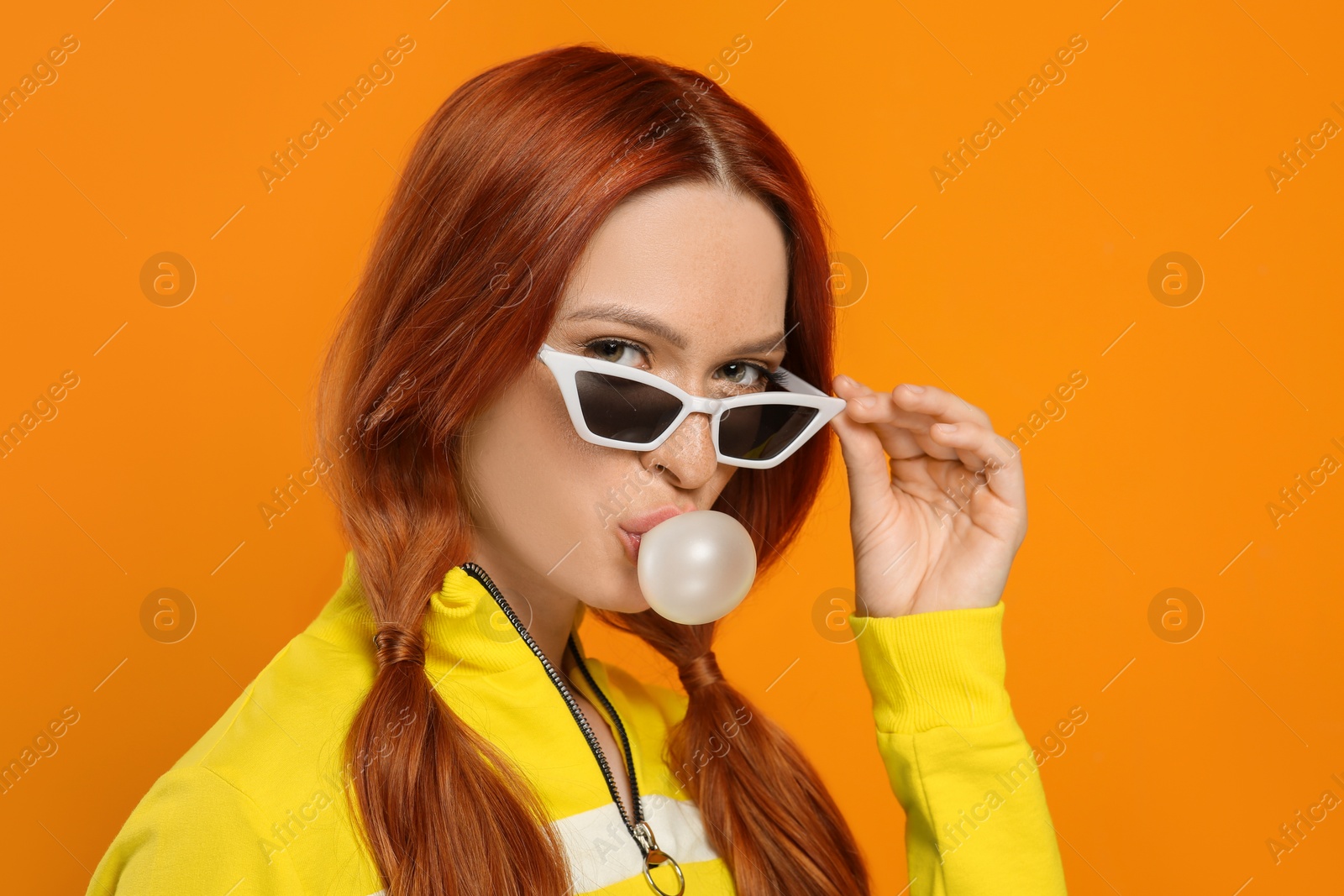 Photo of Portrait of beautiful woman in sunglasses blowing bubble gum on orange background