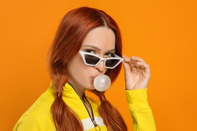 Photo of Portraitbeautiful woman in sunglasses blowing bubble gum on orange background
