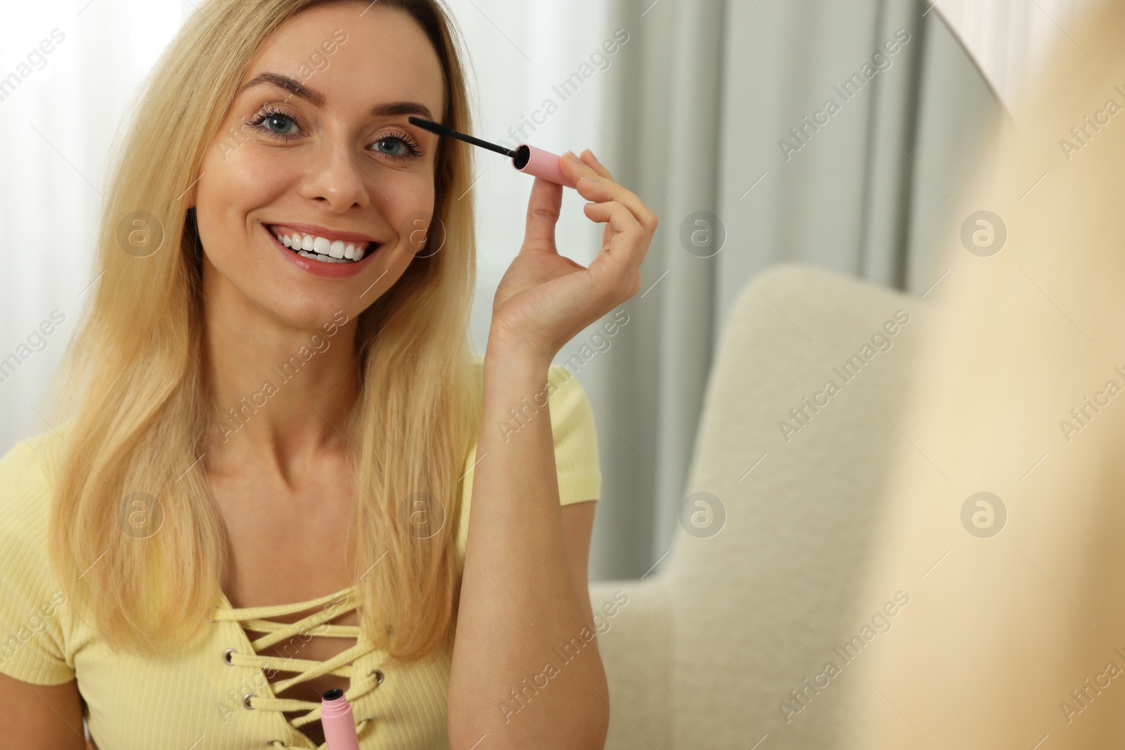 Photo of Beautiful woman applying mascara near mirror at home